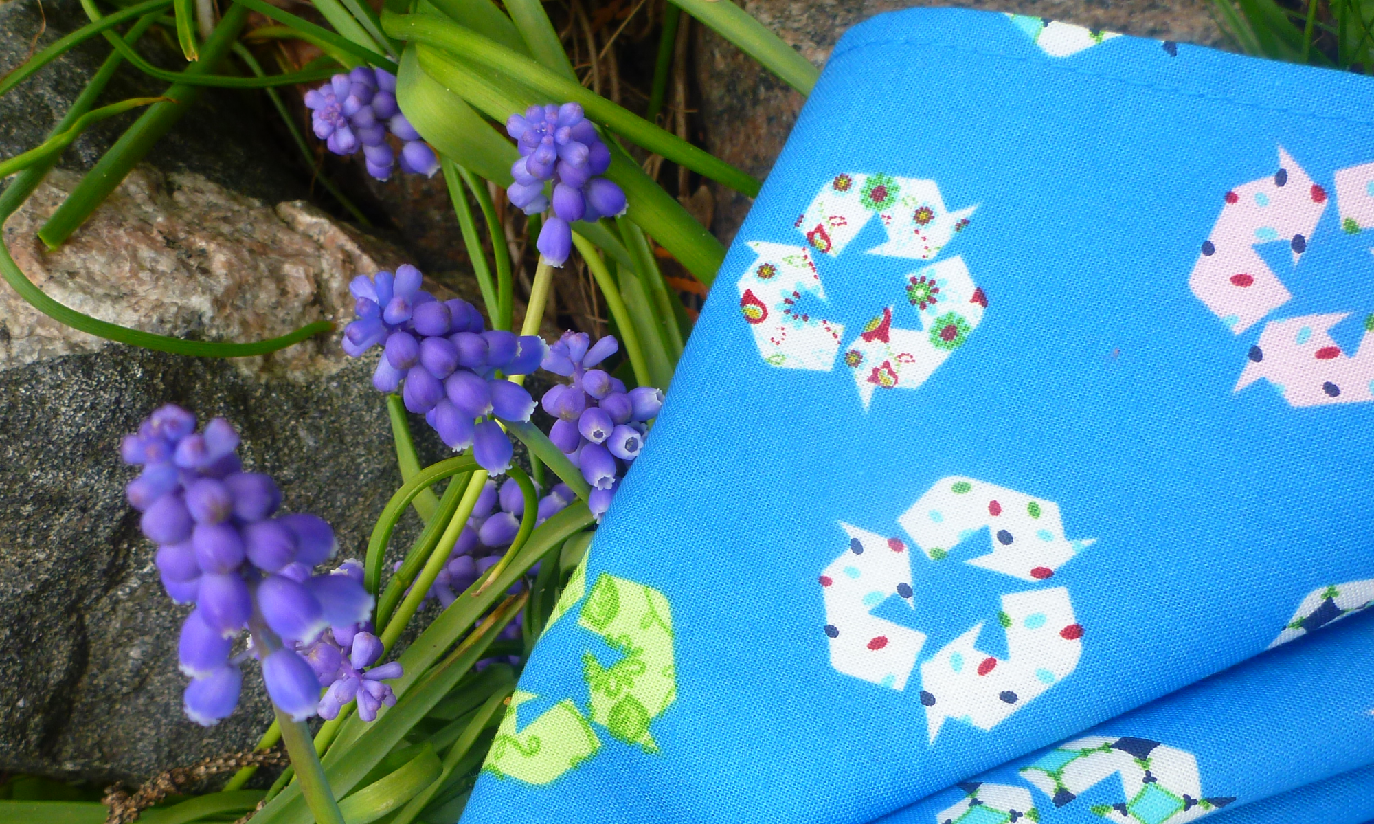 bright blue napkin with pattern of recycling logos, lying in grass with flowers.